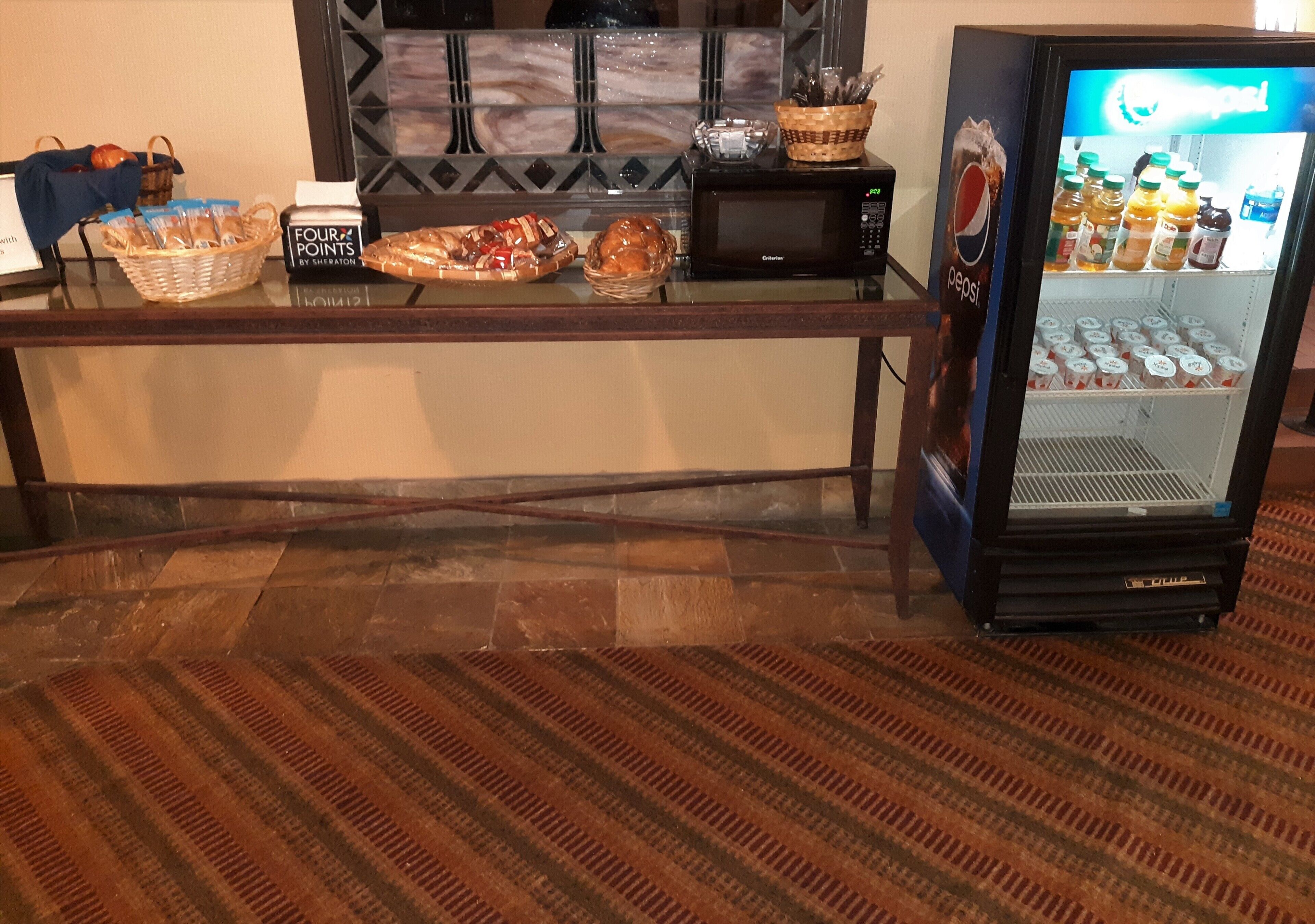 Een hotel receptie met een magnetron, koelkast en diverse etenswaren op een toonbank.