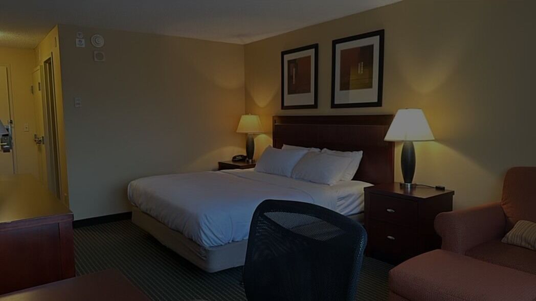 A hotel room with a bed, two bedside tables, a chair, a desk, and a door.