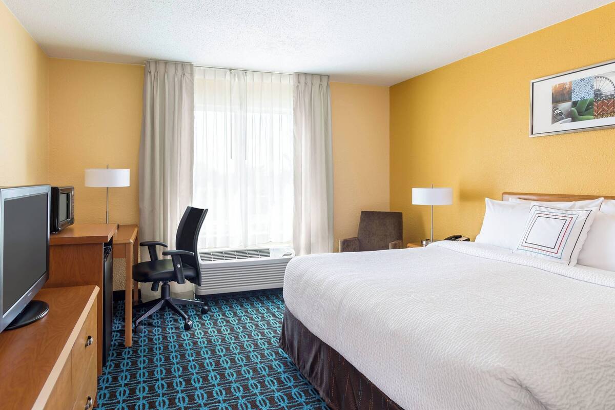 A hotel room with a bed, desk, chair, TV, and a window with curtains.
