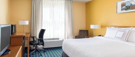 Une chambre d’hôtel équipée d’un lit, d’un bureau, d’une chaise, d’une télévision et d’une fenêtre avec des rideaux.