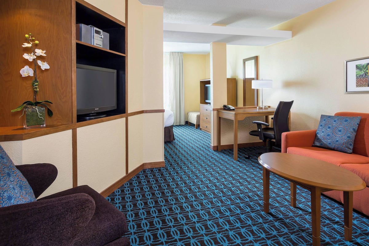 A hotel room with a TV, a desk, a sofa, and a patterned carpet.