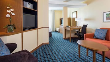 Habitación de hotel con televisión, escritorio, sofá y alfombra estampada.