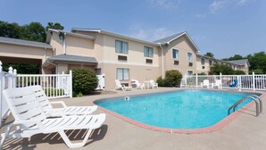 Piscina com espreguiçadeiras e cerca, cercada por um edifício com várias janelas e varandas.