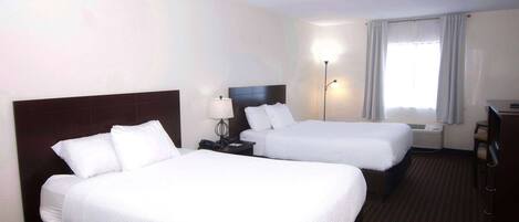 A hotel room with two beds, a desk, a lamp, and a window with curtains.