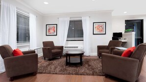 Uma sala de estar com duas poltronas marrons, uma mesa de centro redonda e uma TV sobre um móvel.