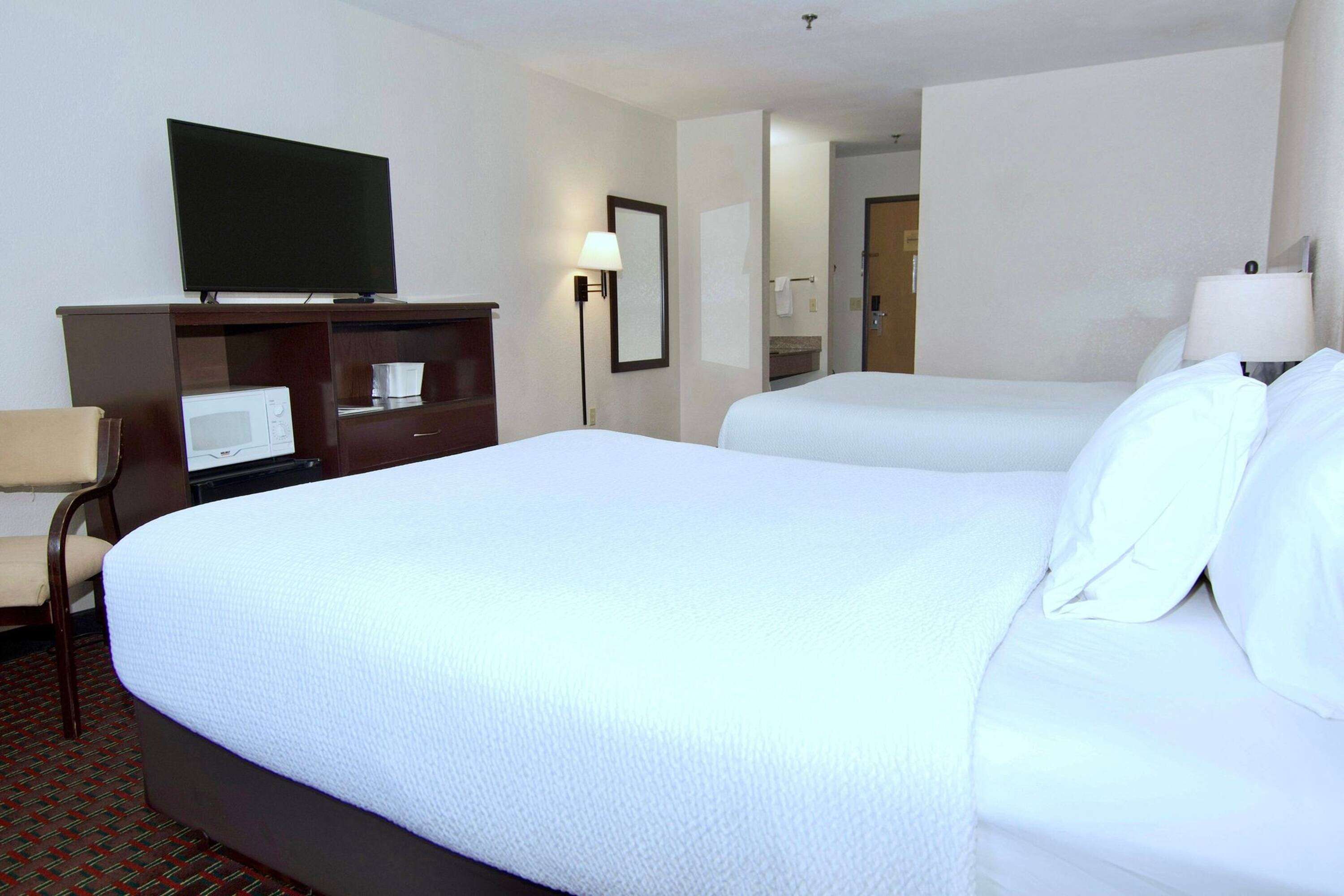 A hotel room with a large bed, a television on a dresser, a microwave, and a desk.