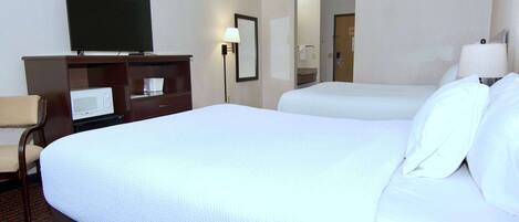 A hotel room with a large bed, a television on a dresser, a microwave, and a desk.