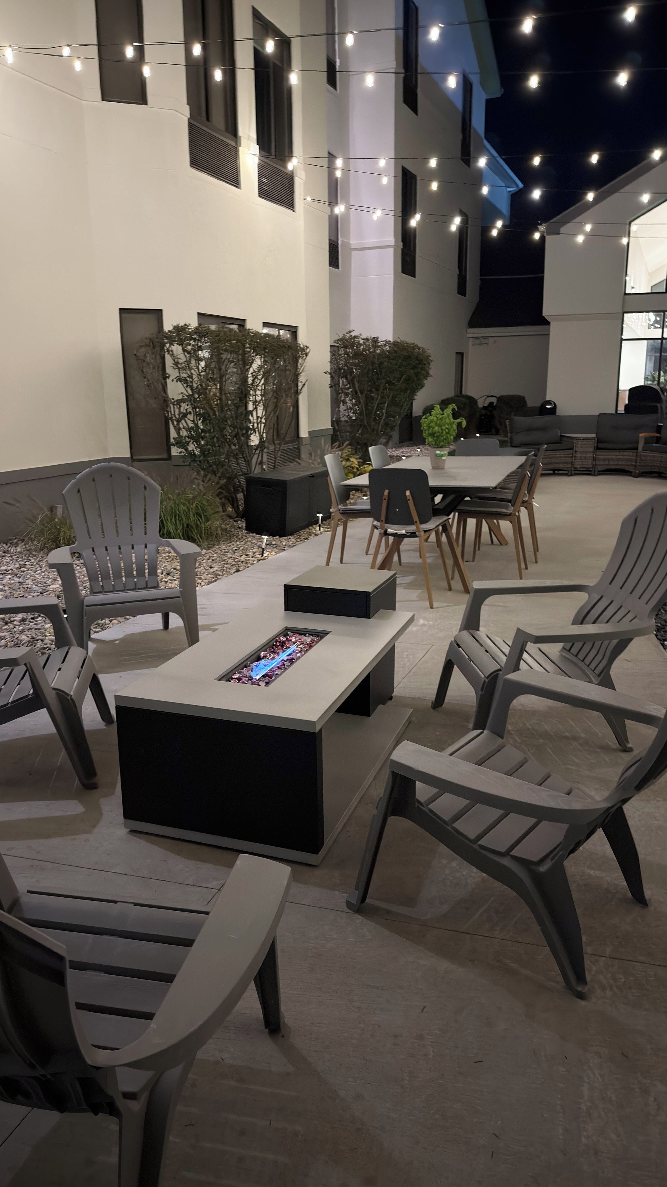 Un espacio al aire libre con mobiliario moderno, que incluye sillas y una mesa, y un elemento decorativo de fuego.