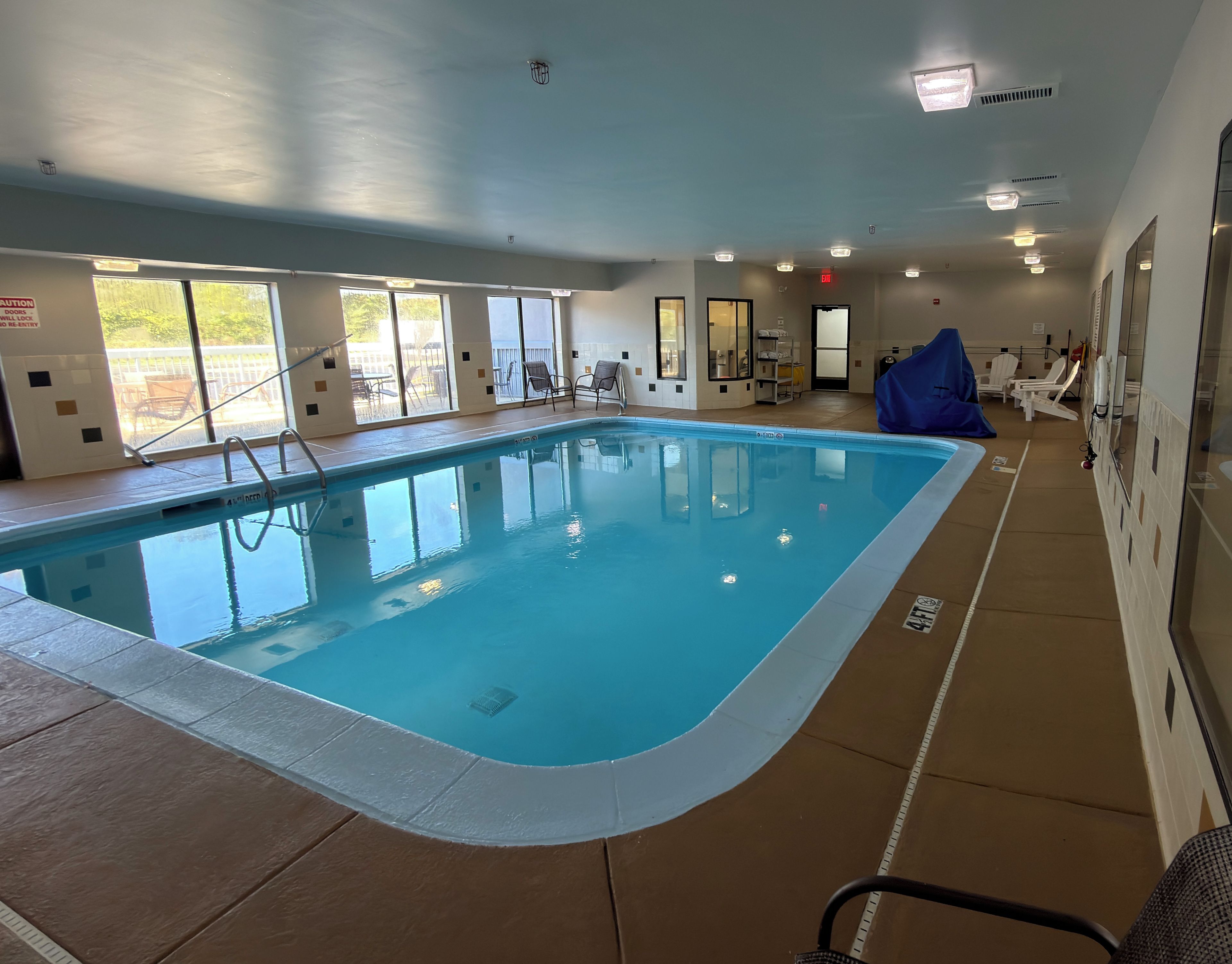 An indoor swimming pool with clear water, surrounded by windows and chairs.