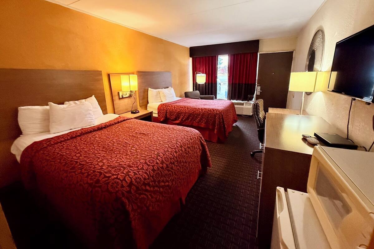 A hotel room with two beds, a TV, a desk with a computer, and a window with curtains.