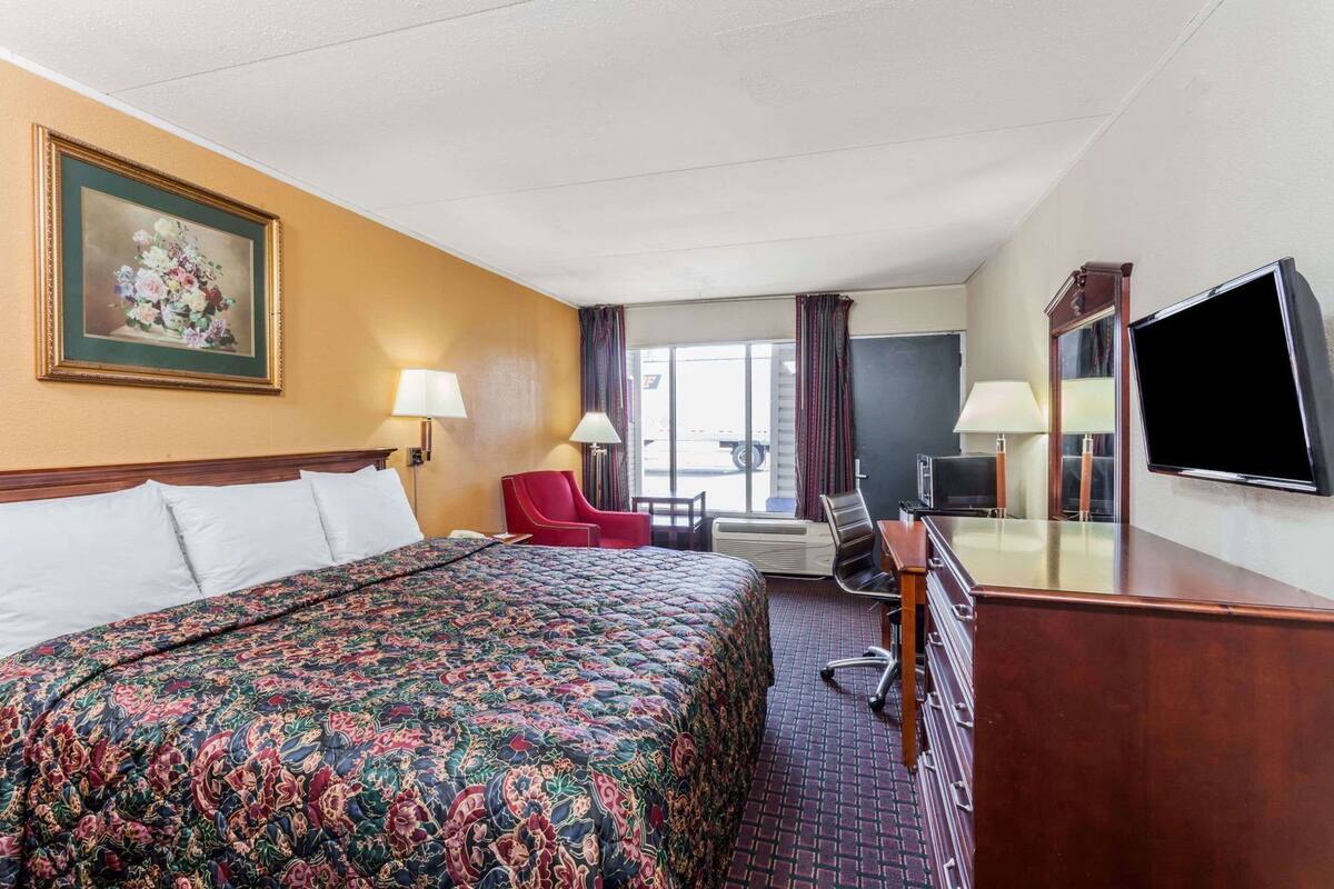 A hotel room with a bed, a desk, a chair, a television, and a window with curtains.