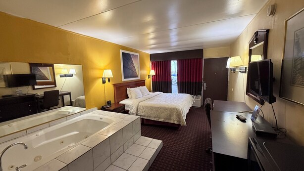 A hotel room with a large bed, a separate desk, a television, a bathroom with a bathtub, and a window with curtains. - Days Inn by Wyndham Seymour (Seymour)