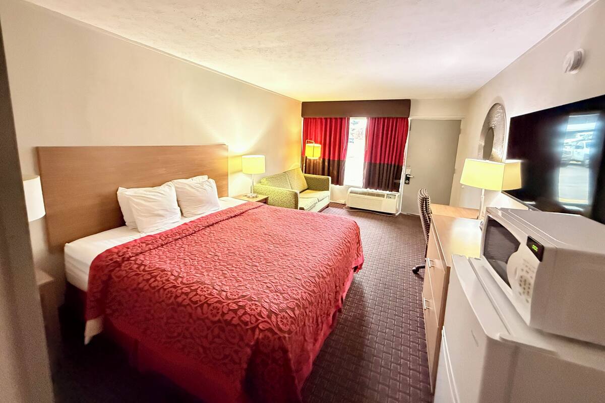 A hotel room with a bed, a desk, a television, and a window with curtains.