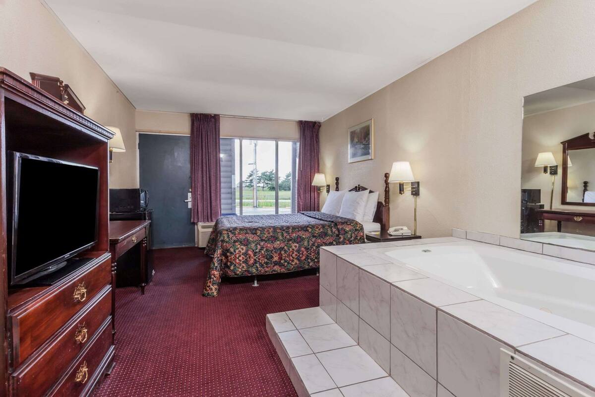 A hotel room with a bed, a TV, a desk, a bathroom with a bathtub, and a large window.