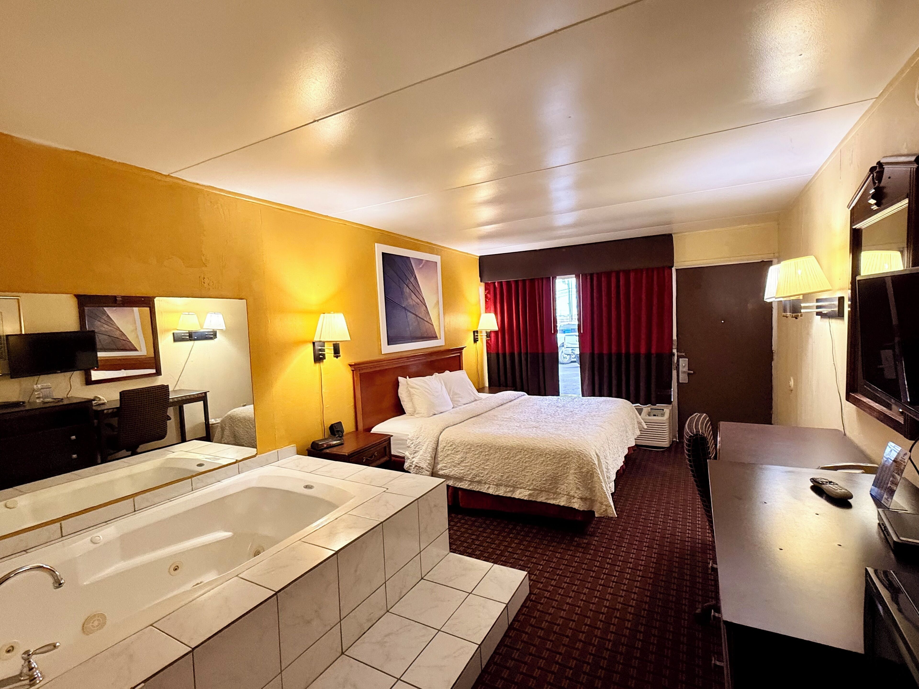 Une chambre d’hôtel avec un grand lit, un bureau séparé avec une chaise, une télévision, une lampe de bureau, un téléphone et une baignoire.