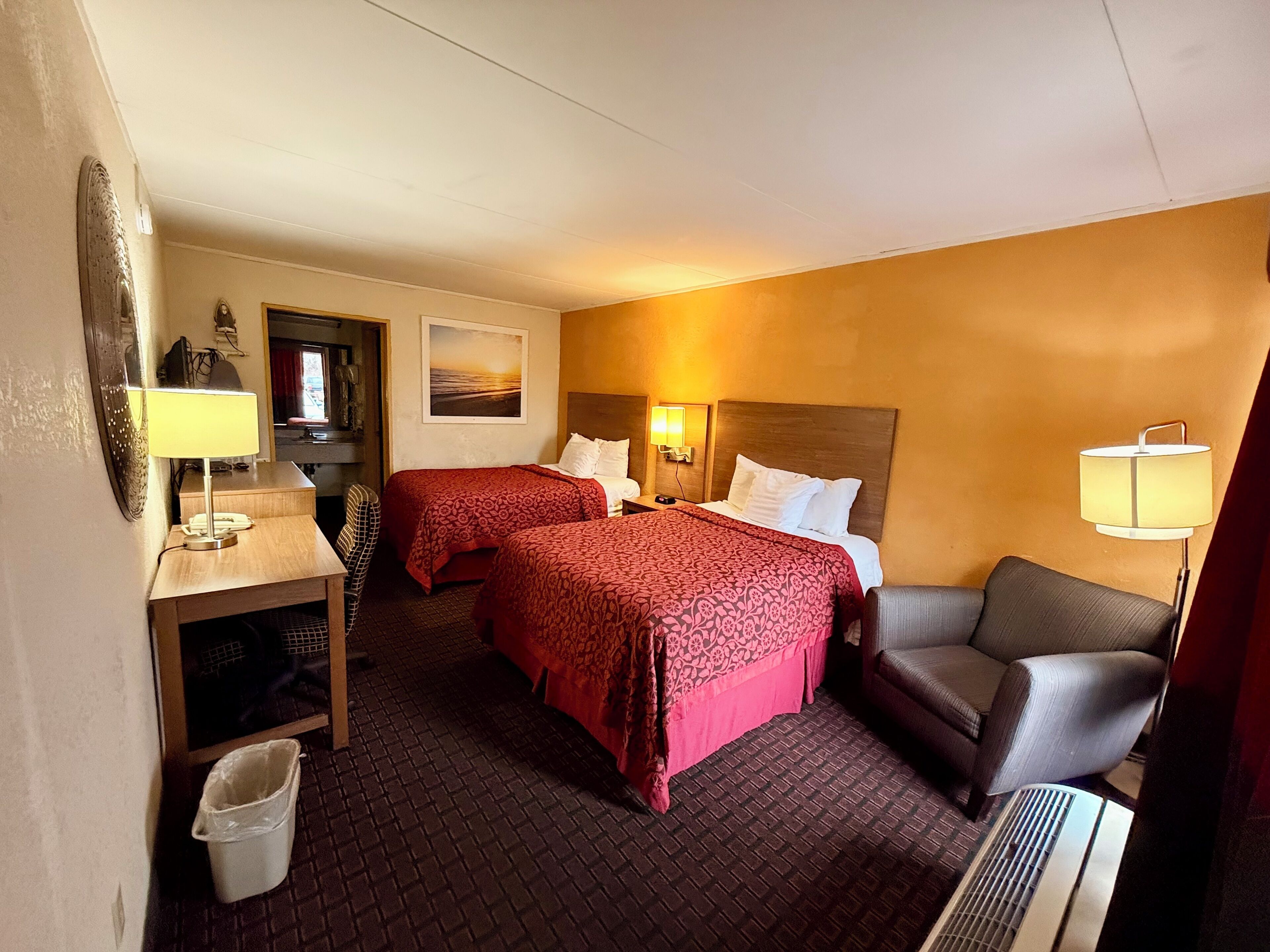 Une chambre d’hôtel avec deux lits, un bureau, une chaise, une poubelle et un radiateur.