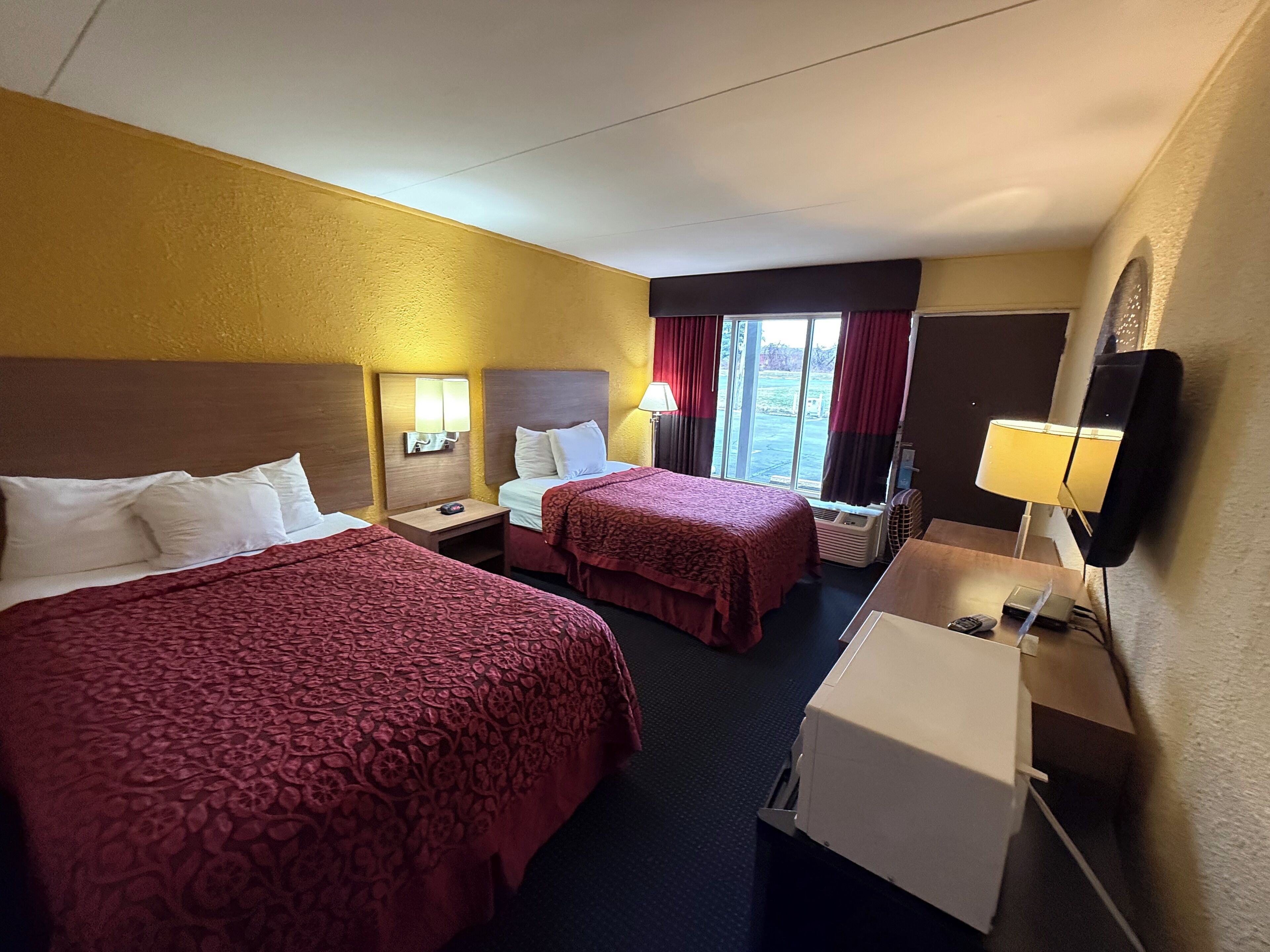 A hotel room with two beds, a desk, a chair, a lamp, and a window with curtains.