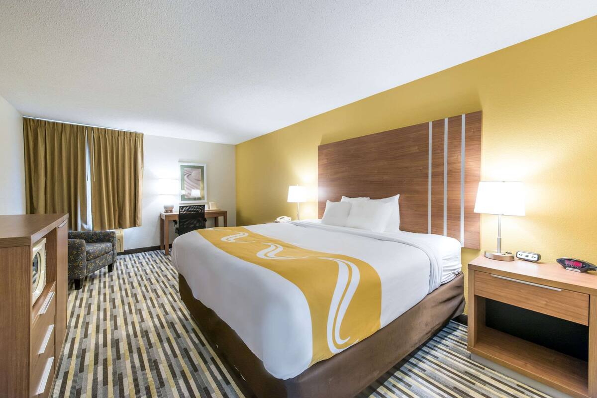 A hotel room with a bed, bedside tables, a desk, and a chair.