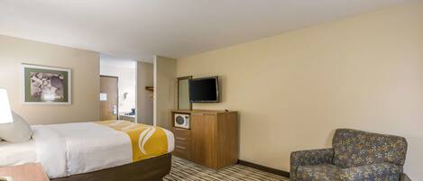 A hotel room with a bed, a chair, a TV, a desk with a phone, and a patterned carpet.