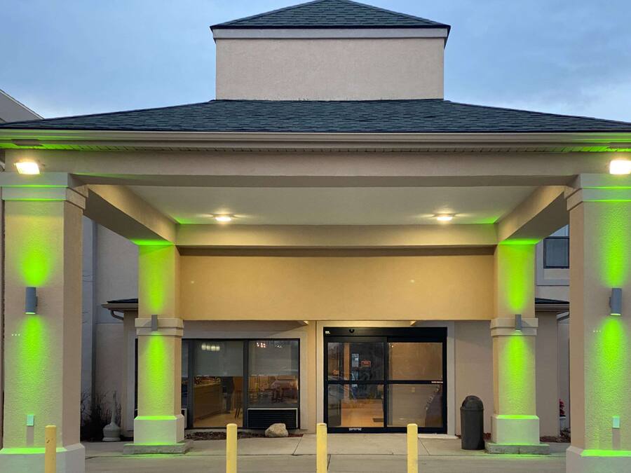 A hotel entrance with a covered walkway, large glass doors, and green lighting.