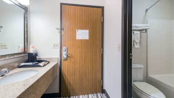 A hotel bathroom with a wooden door, a sink with a mirror, and a toilet with a towel rack.