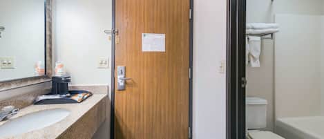 A hotel bathroom with a wooden door, a sink with a mirror, and a toilet with a towel rack.