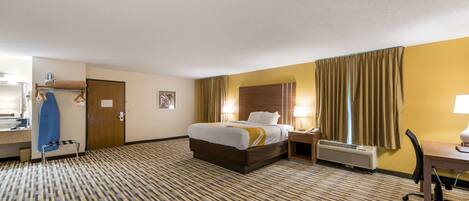 A hotel room with a bed, bedside table, lamp, and a desk with a chair.