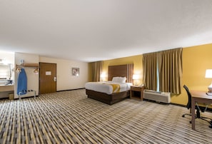 A hotel room with a bed, bedside table, lamp, and a desk with a chair.