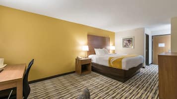 Una habitación de hotel con cama, mesita de noche, lámpara, silla y escritorio con una taza.