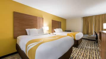 Habitación de hotel con dos camas, un escritorio, una silla y un amplio ventanal con cortinas.
