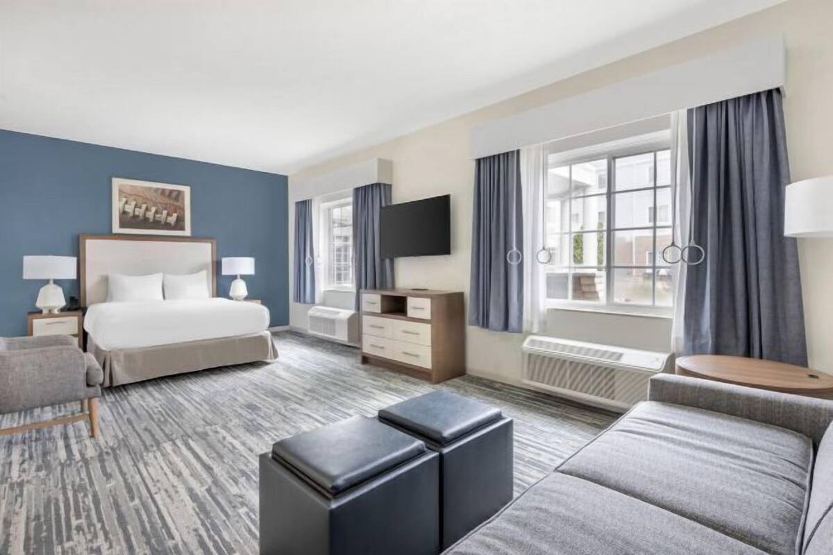 A hotel room with a bed, a sofa, a TV, a desk, and a window with curtains.