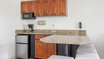 A compact kitchen with wooden cabinets, a built-in microwave, a coffee maker, and a granite countertop.