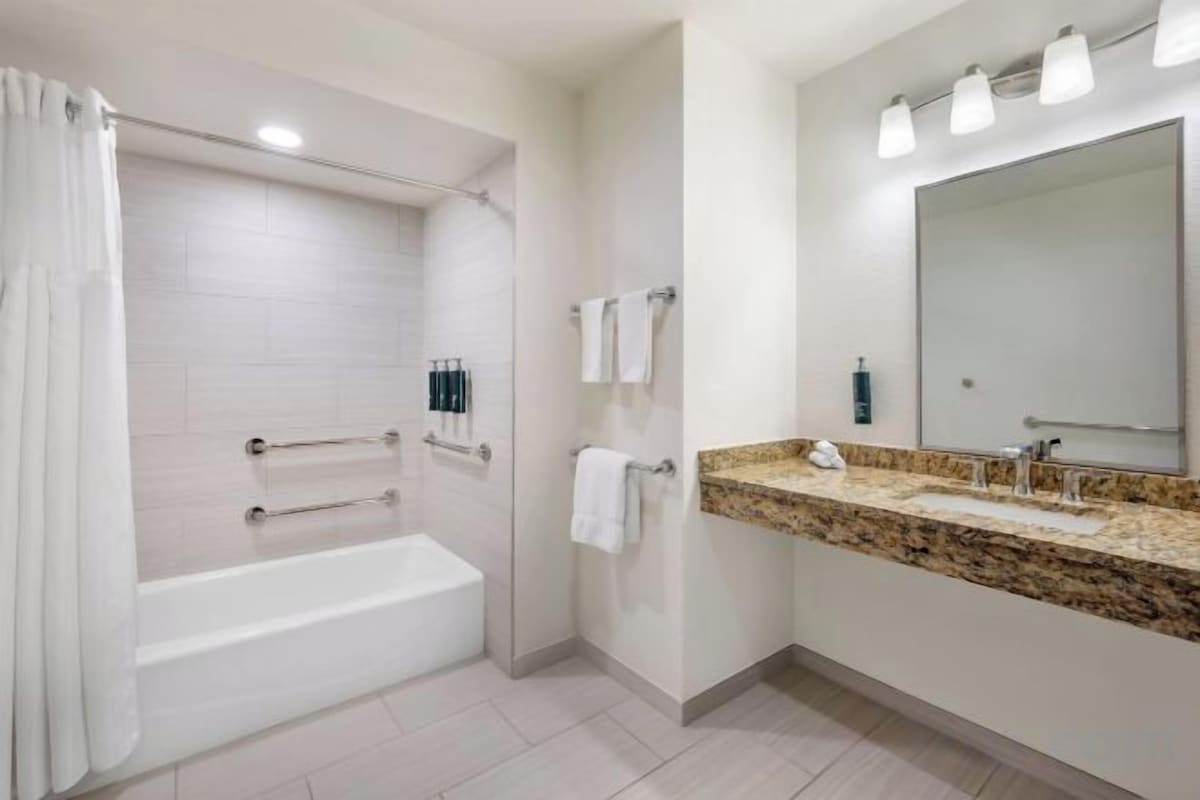 Un baño con bañera, lavamanos con encimera de granito, un espejo grande y cortina de ducha.