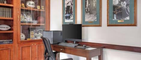Ein Arbeitsraum mit einem Holztisch, einem Computer und gerahmten Fotos an der Wand.