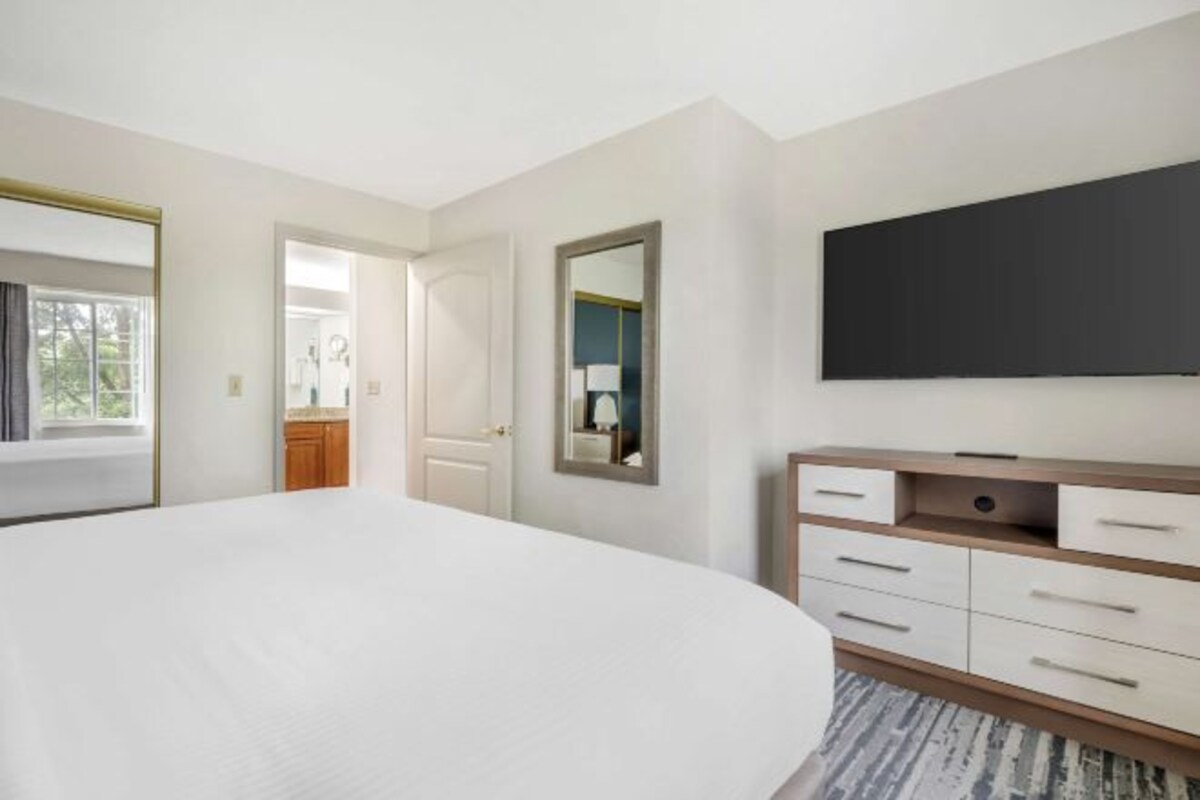 Un dormitorio con una cama grande, un aparador, un espejo y un televisor en la pared.