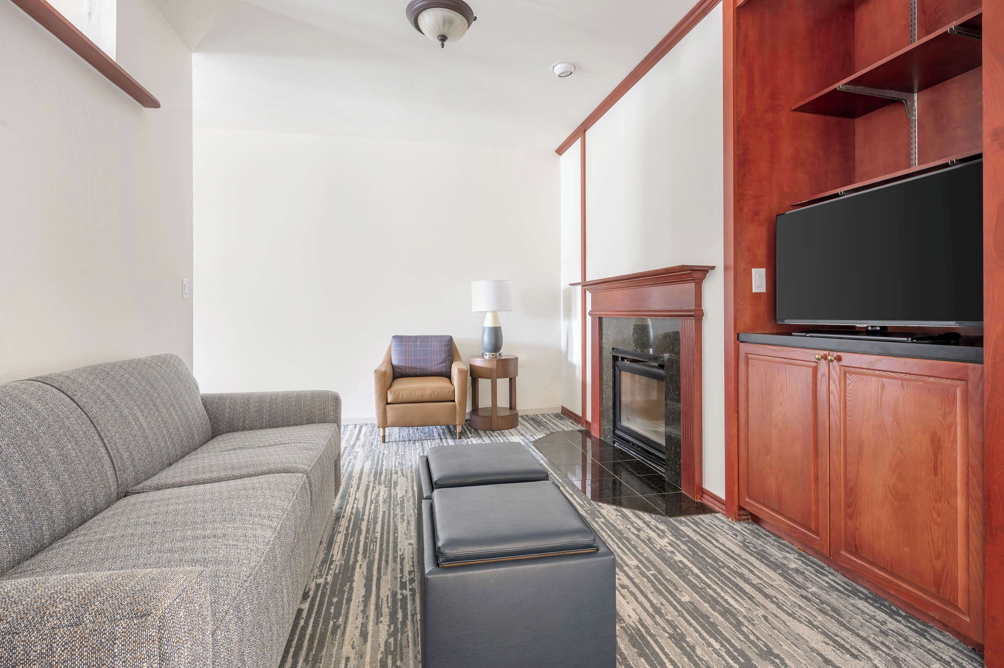 Una sala de estar moderna con un sofá gris, una mesita auxiliar con una lámpara, una chimenea y un televisor de pantalla plana grande.