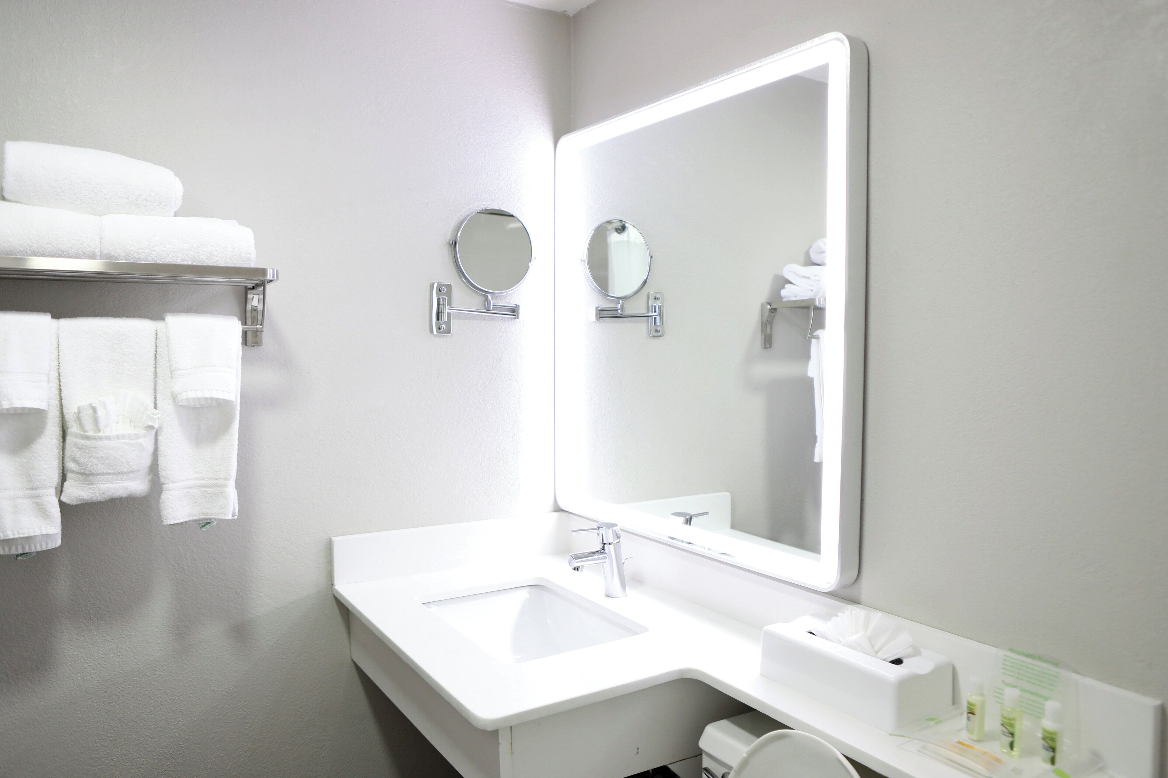 A modern bathroom with a white sink, a large mirror, and a towel rack with neatly folded towels.
