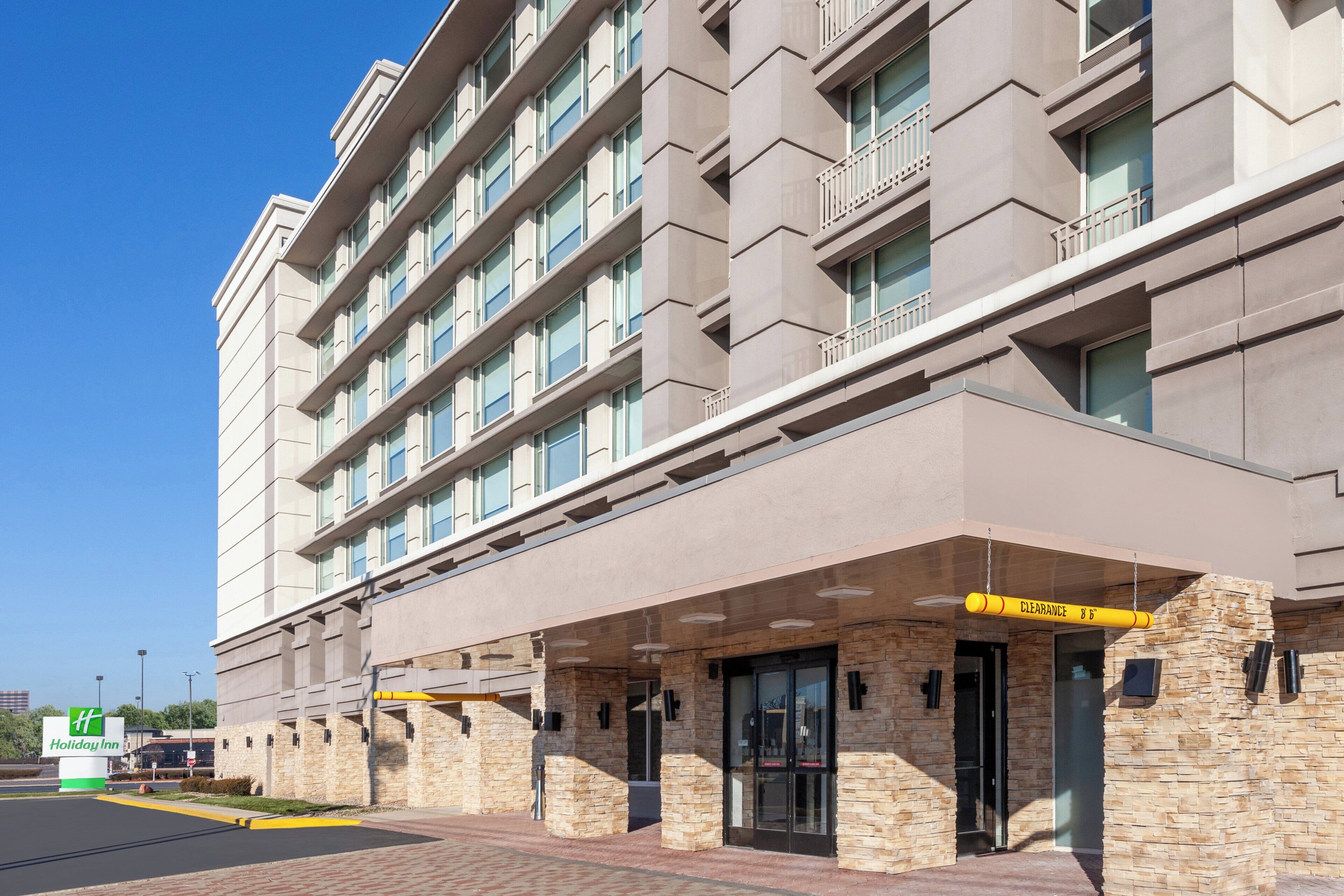 A multi-story hotel with a stone facade, a covered entrance, and a clear sky.