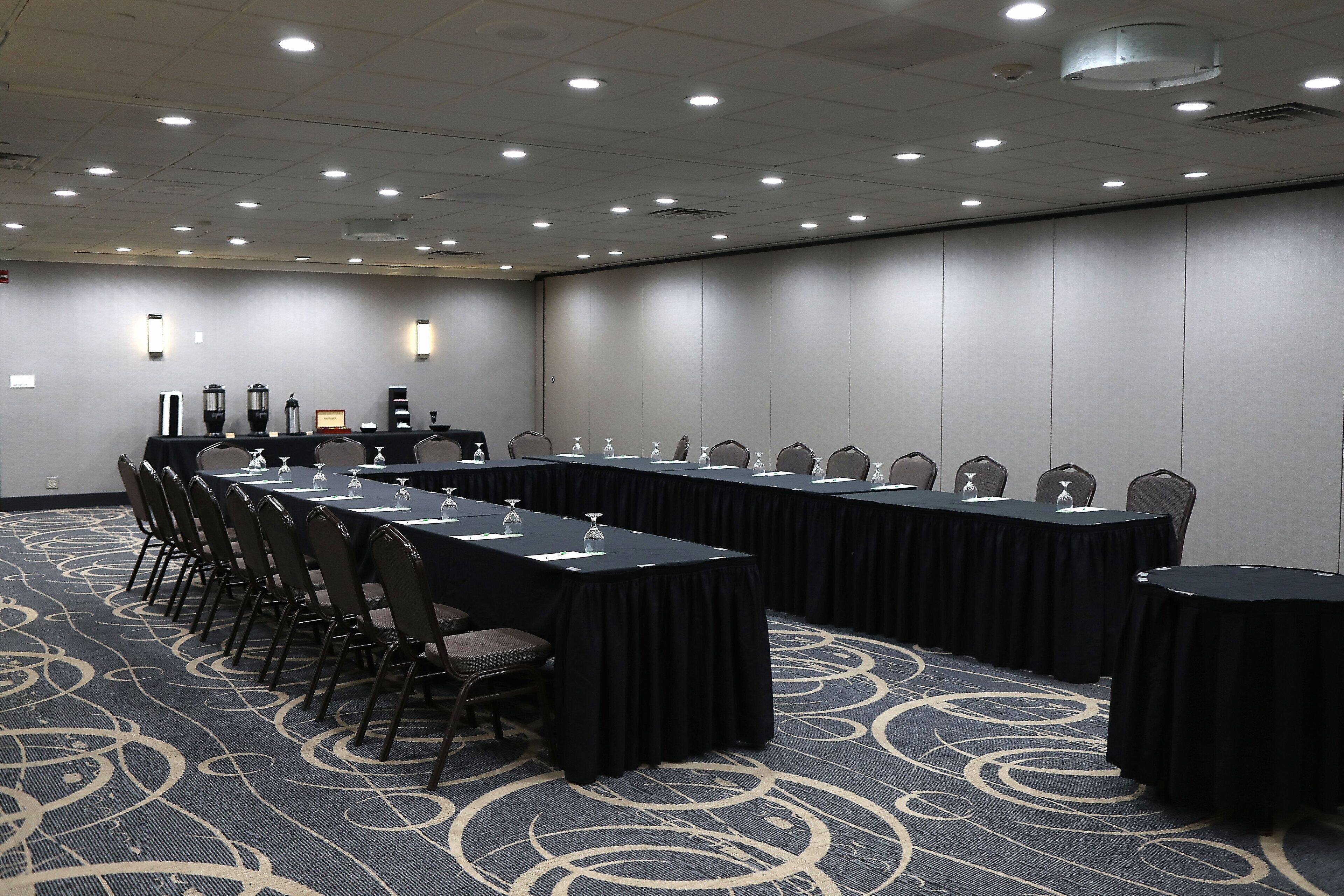 Una sala de conferencias con mesas largas, sillas y piso alfombrado.