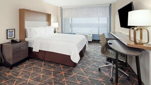 A hotel room with a bed, desk, chair, TV, and a large window with a city view. - Holiday Inn Chicago Oakbrook by IHG (Oakbrook Terrace)