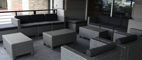 A patio area with wicker furniture, including sofas and ottomans, arranged on a tiled floor.