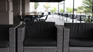A covered outdoor seating area with wicker furniture and a view of the street. - Holiday Inn Chicago Oakbrook by IHG (Oakbrook Terrace)