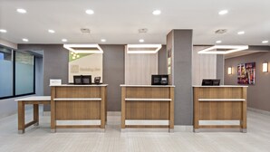 A reception area with three wooden reception desks, a glass wall on the left, and a colorful artwork on the right. - Holiday Inn Chicago Oakbrook by IHG (Oakbrook Terrace)