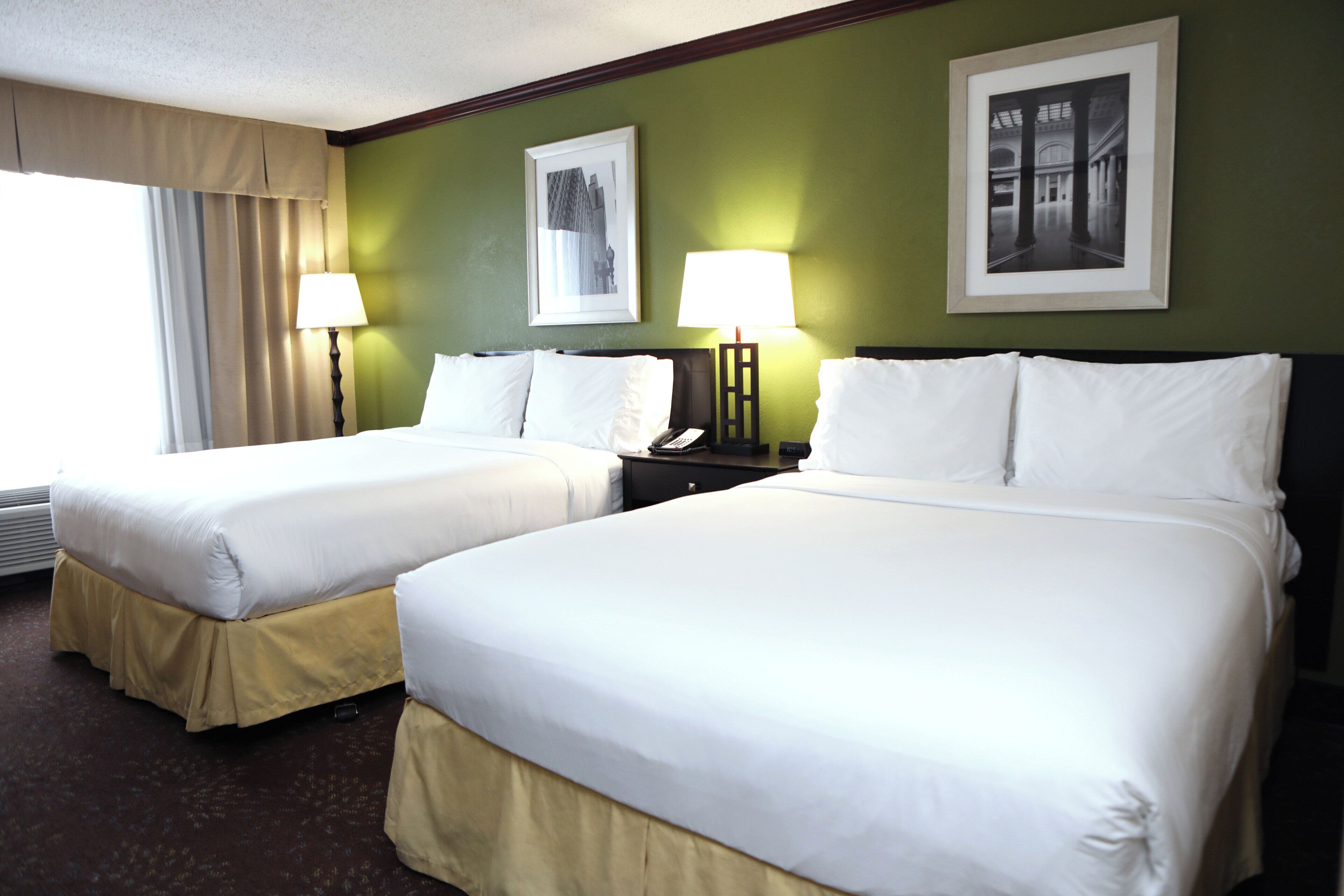 A hotel room with two beds, a window with curtains, and two wall-mounted lamps.
