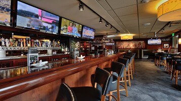 Un bar con múltiples pantallas mostrando eventos deportivos, una variedad de grifos de cerveza y un área de asientos con taburetes de bar.