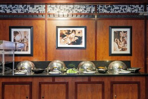 A kitchen counter with three large silver food covers, a framed photograph on the wall, and a tiled backsplash.