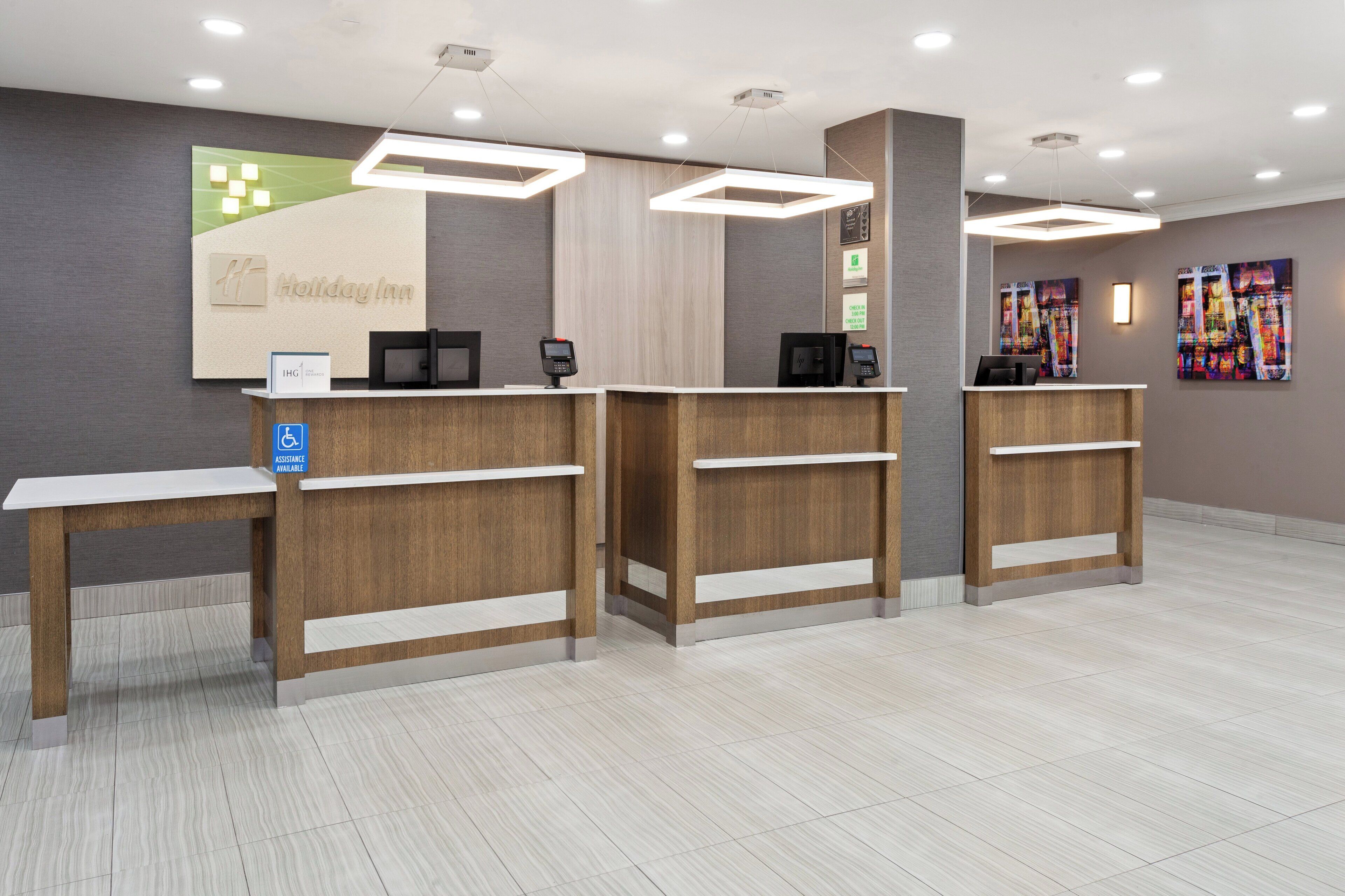 Un área de recepción con un mostrador de madera, una pantalla digital y un cartel que indica acceso para sillas de ruedas.