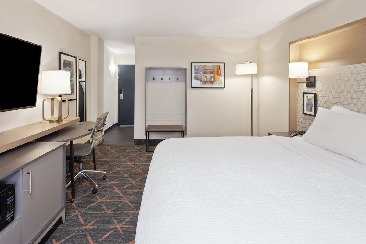 A hotel room with a bed, desk, chair, TV, and artwork on the walls.