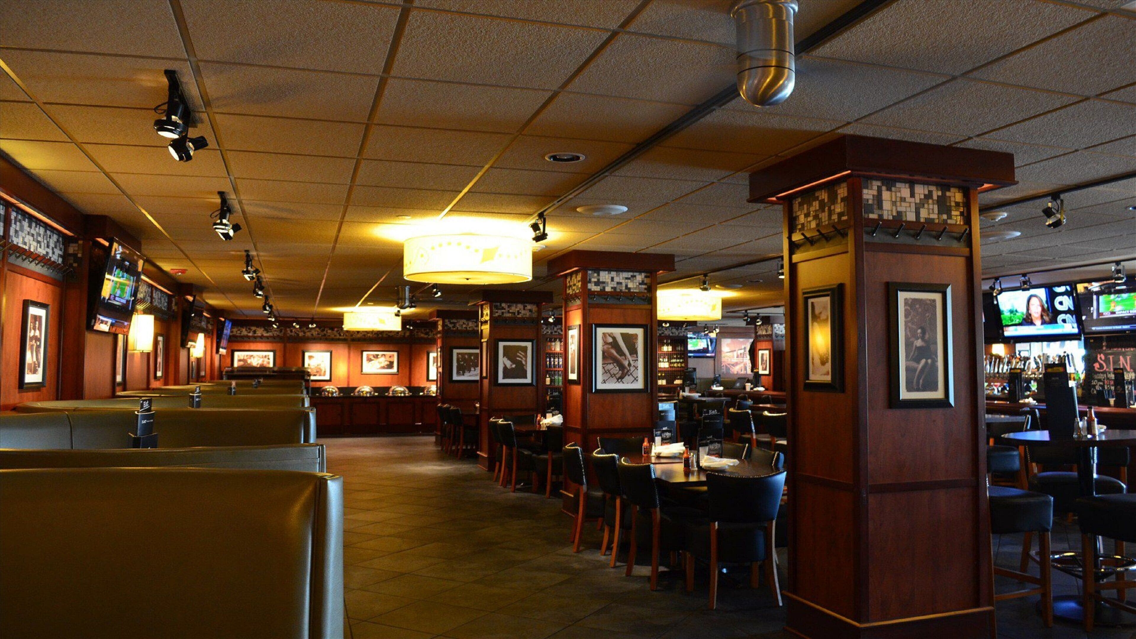 A restaurant with booths and tables, ceiling lights, and wall-mounted TVs.