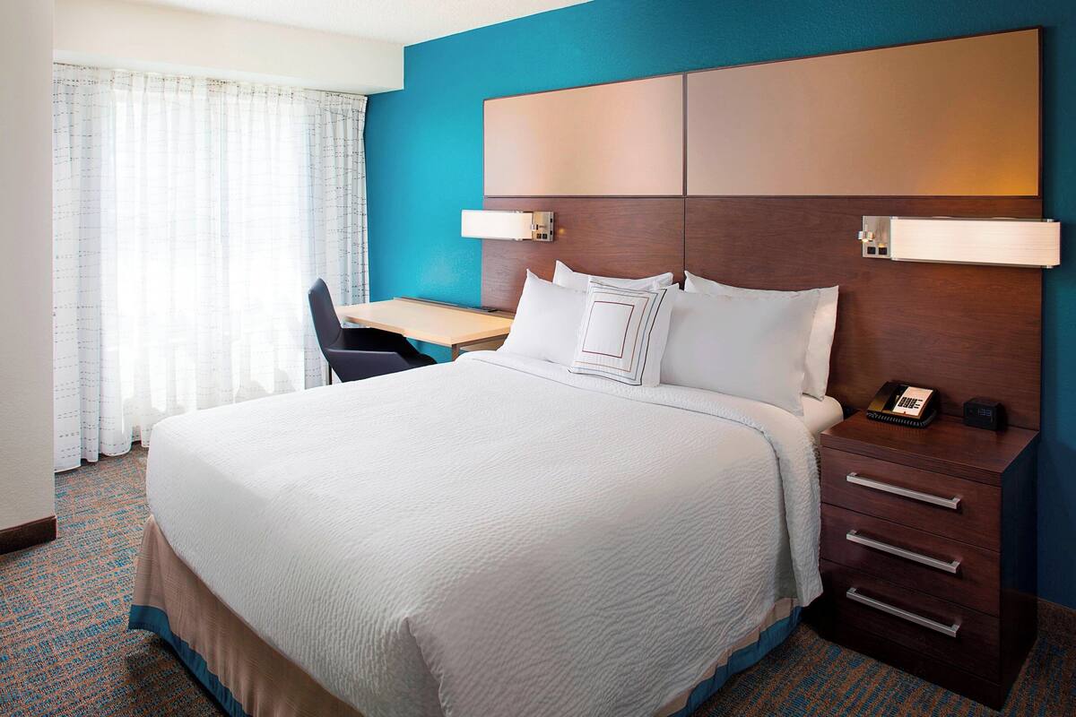 Una habitación de hotel con una cama grande, un escritorio y una mesita de noche.